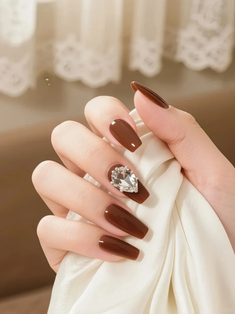 Long brown manicure with rhinestone nail accent and soft glow
